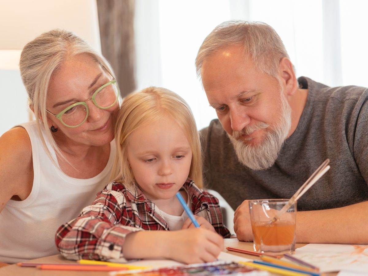 Des grands-parents dessinent avec leur petite-fille autour de la table