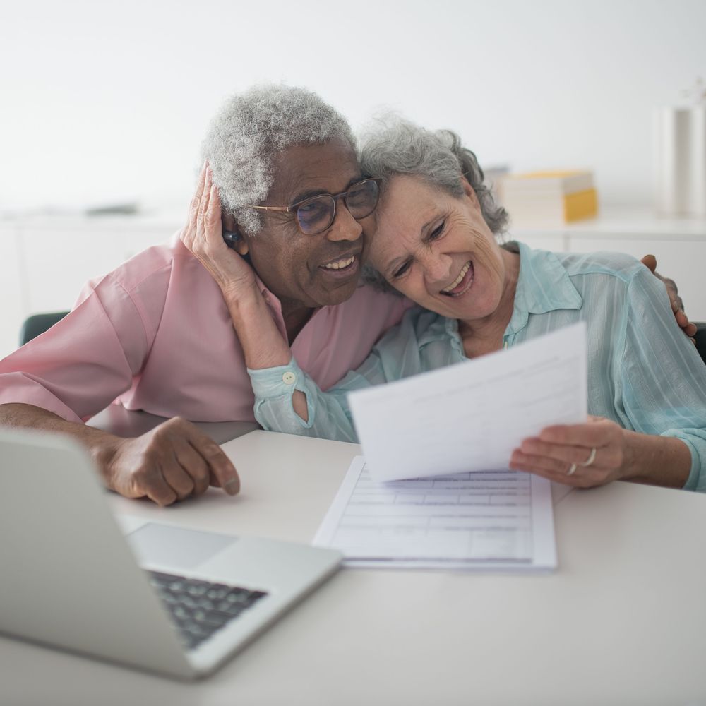 Un couple de retraités, souriant, relit ses documents à la maison